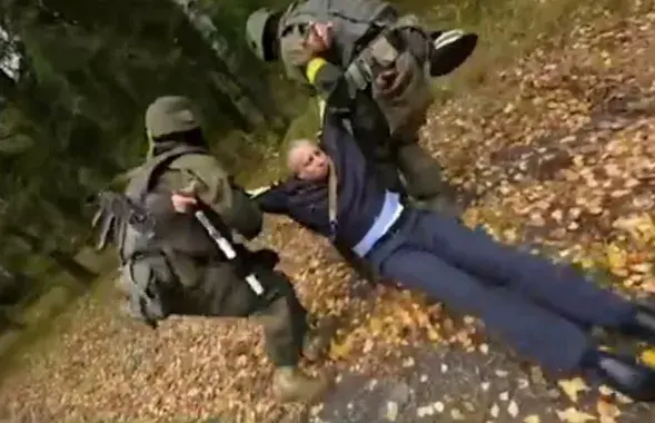 Байцы з жоўтымі павязкамі цягнуць "забітага" міліцыянера ў лес / Скрыншот з відэа МУС
