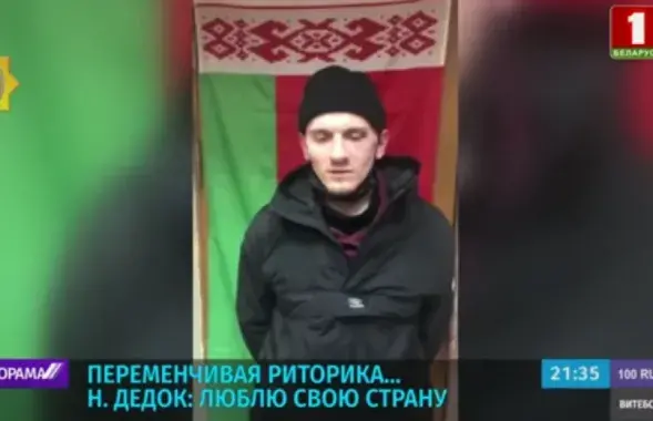 Николай Дедок после задержания на фоне красно-зелёного флага / Скриншот с видео, показанного на телеканале "Беларусь 1"​